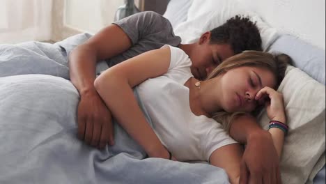Close-Up-view-of-multiracial-couple-lying-in-bed-and-sleeping-while-embracing-each-other.-Young-family-concept