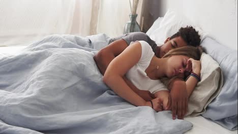 Multiracial-couple-lying-in-bed-and-sleeping-while-embracing-each-other.-Young-family-concept