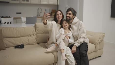 Eine-Glücklich-Lächelnde-Familie-Macht-Mit-Einem-Smartphone-Auf-Einem-Sofa-Im-Wohnzimmer-Ein-Selfie-Oder-Einen-Videoanruf