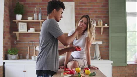 Happy-multi-ethnic-couple-chatting-in-the-kitchen-early-in-the-morning.-Handsome-man-feeding-his-wife-while-cooking-breakfast