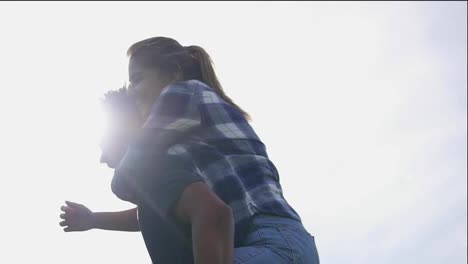 Close-Up-view-of-a-handsome-african-guy-piggybacking-his-caucasian-happy-girlfriend-against-the-son.-Lens-flare