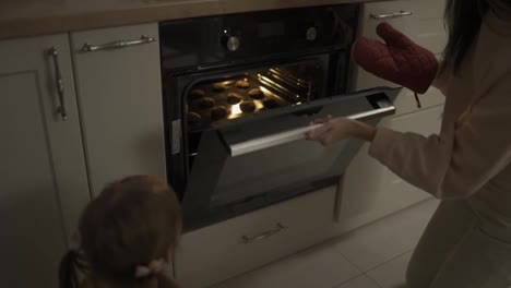 Mother-and-daughter-are-taking-out-cakes-from-the-oven-in-the-kitchen