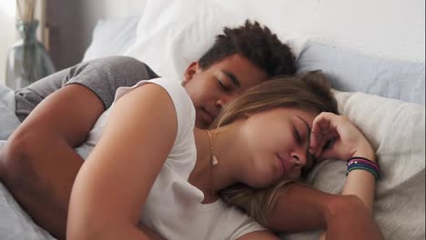 Close-Up-view-of-multiracial-couple-lying-in-bed-and-sleeping-while-embracing-each-other.-Young-family-concept