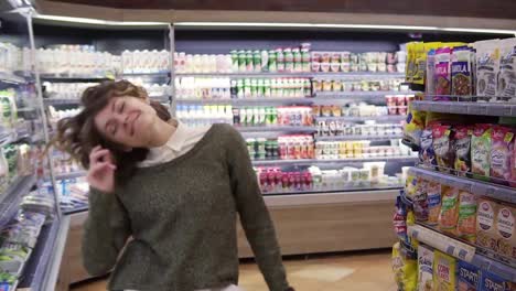 Portrait-of-young-woman-with-shirt-curly-hair-dancing-standing-at-grocery-store-aisle.-Excited-woman-having-fun,-dancing