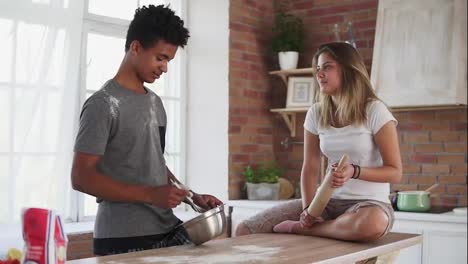 Young-multi-ethnic-couple-cooking-together-in-the-kitchen.-Attractive-african-man-mixing-ingredients-in-a-pot.-His-girlfriend-is
