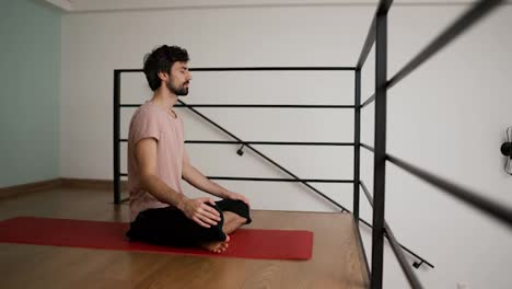 Side-view-of-a-man-meditating-at-home-with-closed-eyes-sitting-on-yoga-mat