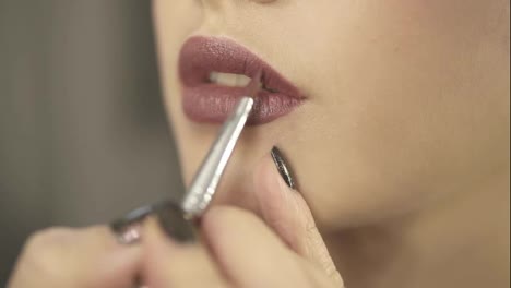 Close-Up-view-of-a-professional-makeup-artist's-hand-using-special-brush-to-apply-lipstick-or-lipgloss-on-model's-lips-working