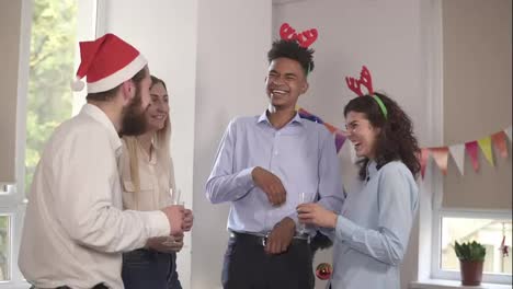 multi-ethnic-group-of-happy-office-workers-holding-glasses-with-sparkling-wine-and-talking-during-christmas-party-in-the-office