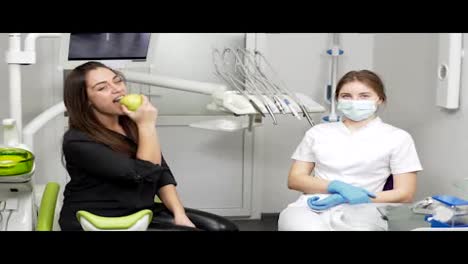 In-Der-Zahnarztpraxis-Beißt-Ein-Mädchen-In-Einen-Grünen-Apfel-Und-Sitzt-Nach-Dem-Eingriff-In-Der-Nähe-Des-Zahnarztes.-Gesunde-Zähne-Und-Gesundes-Lächeln
