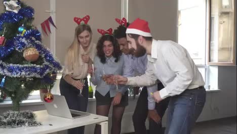 Side-view-of-happy-team-in-santa-hats-making-conference-call-and-clicking-glasses-with-sparkling-wine-at-corporate-office-party