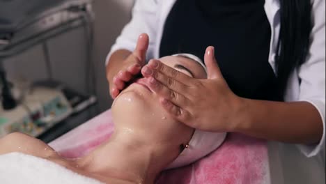 Close-Up-view-of-a-professional-cosmetologist-hands-making-face-and-neck-massage-in-spa-salon.-Young-woman-is-lying-on-the