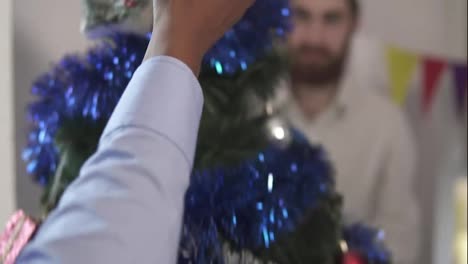 Close-Up-view-of-and-african-american-hand-putting-a-decoration-on-the-top-of-the-little-artificial-Christmas-tree-decorated-by