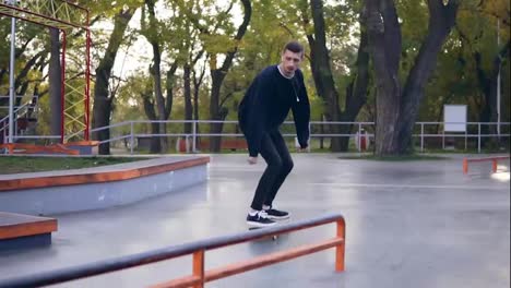 Extreme-skateboarder-listening-to-the-music-in-earphones-grinding-down-rail-in-the-skatepark.-Slow-Motion-shot