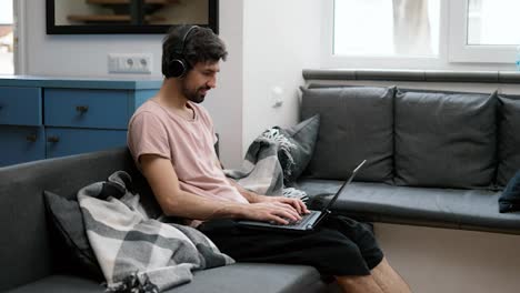 Hombre-Caucásico-Con-Auriculares-Escribiendo-En-Una-Computadora-Portátil-En-Casa,-Cansado-Terminando-El-Trabajo