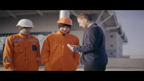 Manager-in-a-suit-giving-envelopes-with-money-to-workers-in-orange-uniform-and-helmets.-Successful-finish-of-the-project