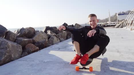 Young-man-sits-at-his-longboard-and-smiles