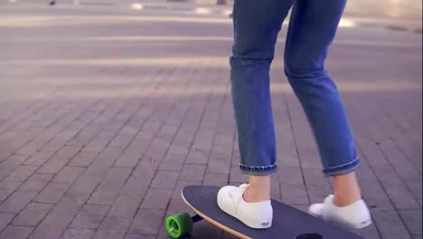 Close-Up-view-of-woman's-legs-in-blue-jeans-and-white-sneakers-starting-to-skateboard-on-the-longboard-in-the-cobblestone-road-in