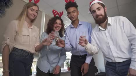 Happy-team-in-santa-hats-making-conference-call-and-clicking-glasses-with-sparkling-wine-at-corporate-office-party.-View-from
