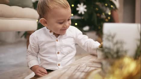 Glücklicher-Süßer-Junge-Im-Weißen-Hemd,-Der-Auf-Dem-Boden-Sitzt,-Mit-Einem-Weihnachtsbaum-Im-Hintergrund