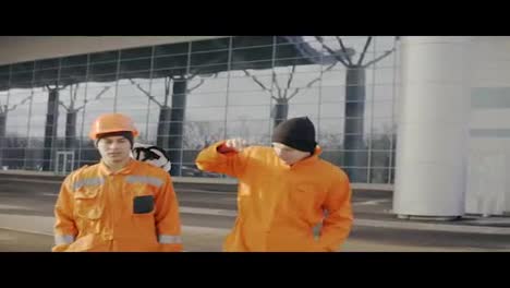 Two-construction-workers-in-orange-uniform-and-helmets-walking-together.-One-of-them-lost-his-helmet.-Having-fun