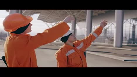 Two-workers-in-orange-uniform-and-helmet-pointing-at-the-building-and-examining-the-object.-Slow-Motion