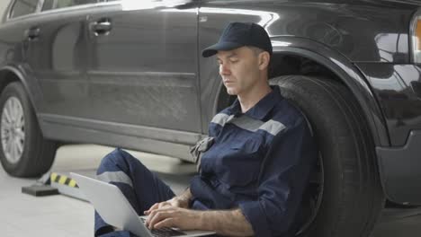 Car-mechanic-working-on-laptop-in-auto-repair-service