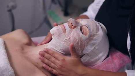 Close-Up-view-of-a-professional-cosmetologist-hands-making-neck-massage-to-the-young-woman-with-mask-on-her-face-and-neck