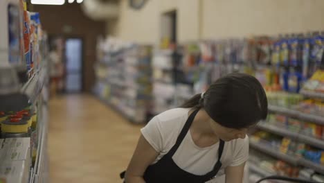 Asian-girl-worker-puts-goods-on-the-shelf.-Filling-shelves-with-goods.-shot-work