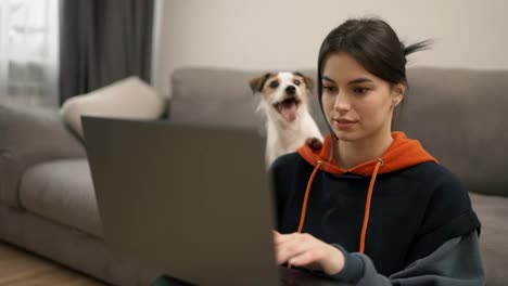 Young-woman-sitting-on-floor-working-on-laptop-with-her-dog-next-her