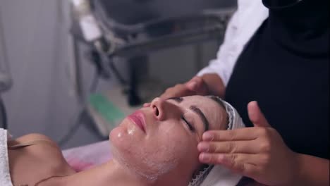 Young-woman-getting-a-professional-peeling-in-spa-salon.-Beautician-hands-at-work,-applying-facial-peeling-on-a-young-girl-face
