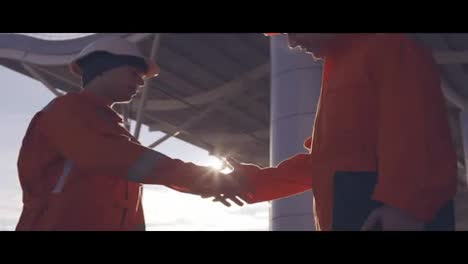 Close-Up-view-of-two-construction-workers-in-orange-uniform-and-hardhats-shaking-hands-at-the-building-object.-Slow-Motion