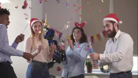 Fröhliche-Multiethnische-Menschen-Mit-Lustigen-Hüten,-Die-Wunderkerzen-Anzünden-Und-Weihnachten-Und-Neujahr-Im-Büro-Feiern,-Aufgeregt-Und-Vielfältig