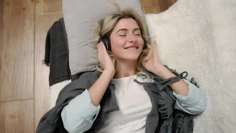 A-smiling-woman-falls-on-a-bed-in-headphones-and-listens-to-music