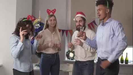 Multiracial-group-of-happy-office-workers-dancing-during-corporate-New-Year-party-wearing-christmas-hats-and-deer-headband