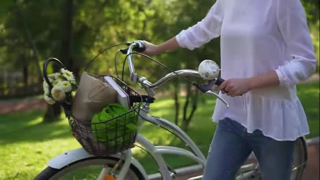 Close-Up-view-of-woman's-hands-holding-a-handlebar-of-a-city-bicycle-with-a-basket-with-flowers-and-book.-Woman-enjoying-her-time