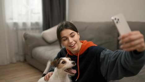 Young-beautiful-woman-taking-selfie-photo-with-dog-and-sitting-on-floor-in-home-interior