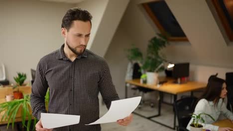 Office-worker-standing-at-modern-office-coworking-space-holding-pile-of-papers