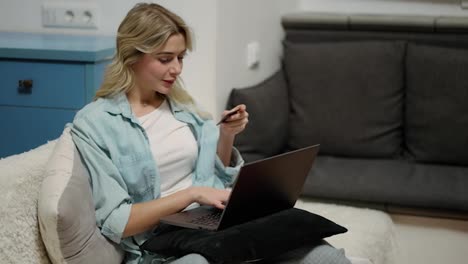 Mujer-Rubia-Sentada-En-Casa-Comprando-En-Una-Tienda-De-Internet-Usando-Una-Computadora-Portátil-Con-Tarjeta-De-Crédito