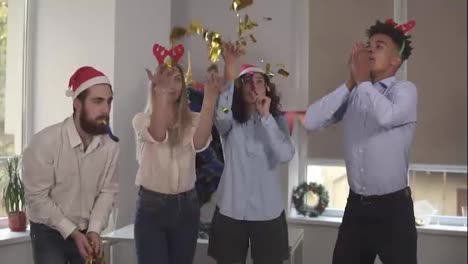 Group-of-multi-ethnic-office-workers-partying-in-the-office-throwing-golden-confetti,-blowing-confetti-from-hands-wearing