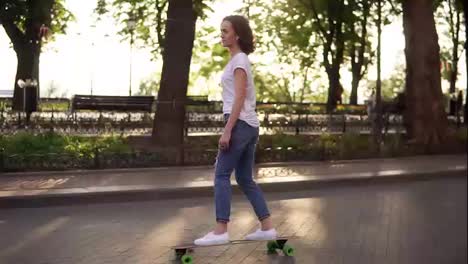 Young-woman-in-blue-jeans-and-white-sneakers-skateboarding-at-sunrise-in-park.-Legs-on-the-skateboard.-Slow-Motion-shot