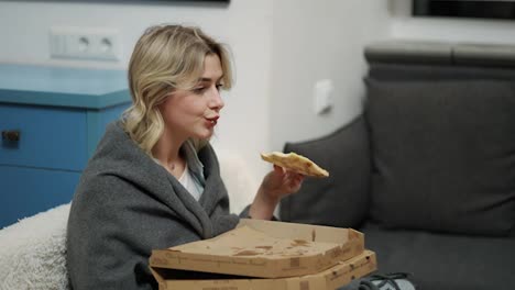 Upset-young-woman-wrapped-in-blanket-taking-pizza-alone