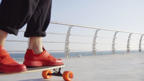 Man-in-red-sneakers-skates-on-longboard-by-the-sea