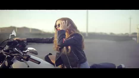 Pretty-female-biker-sitting-on-the-motorcycle-seat.-Close-up-of-young-curly-woman-in-sunglasses-on-the-chopper