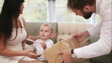 Blonde-cute-toddler-receiving-christmas-present-from-his-father.-But-he-asks-his-mother-to-take-him-on-her-hands.-Family