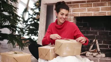 Schöne-Lächelnde-Frau,-Die-Weihnachtsgeschenke-Einpackt,-Zu-Hause-Am-Weihnachtsbaum-Und-Am-Kamin-Sitzt-Und-Sie-Dann-Unterstellt