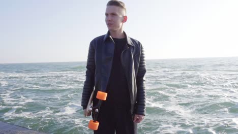 Young-man-holds-his-longboard-standing-by-the-sea