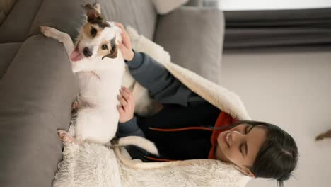 Beautiful-woman-sitting-on-couch-in-blanket-with-her-small-dog-Jack-Russell-terrier