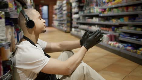 Supermarket-worker-in-apron-sitting-on-the-floor-and-listen-to-the-music