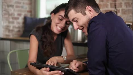 Romantic-young-couple-using-tablet-in-coffee-shot.-Woman's-hands-pointing-at-the-touchscreen
