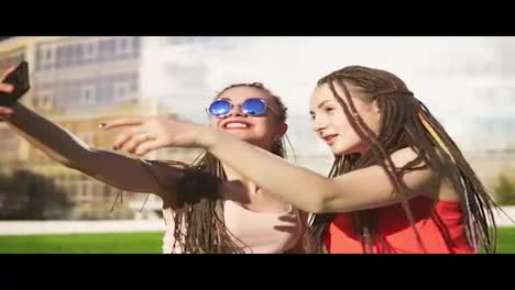 Mujeres-Felices-Con-Rastas-Sentadas-En-El-Césped-En-El-Parque-De-Verano-Y-Hablando-De-Selfies.-Jóvenes-Amigos-Hablando-Y-Tomando-Fotos,-Posando